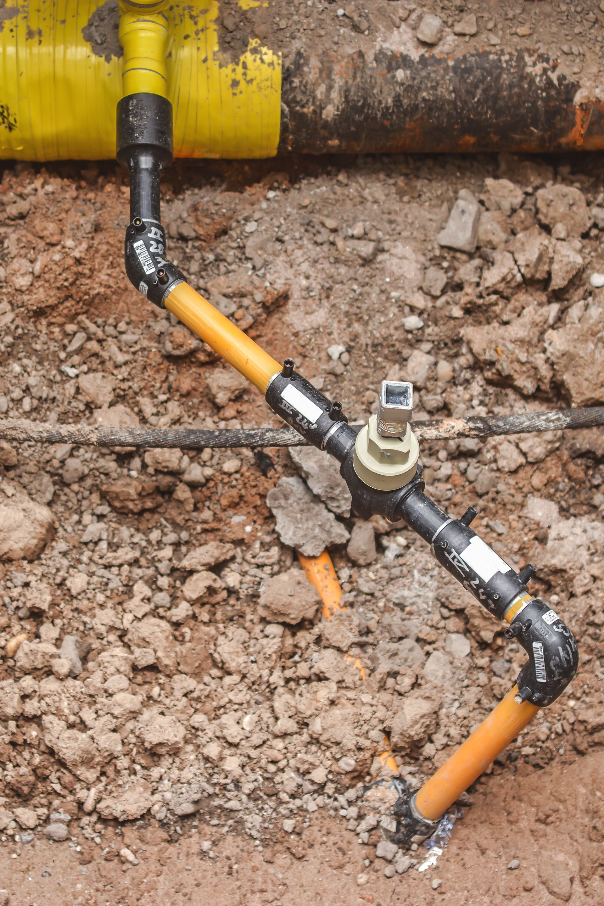 Underground gas pipes with a valve and connections, orange and black against dirt.
