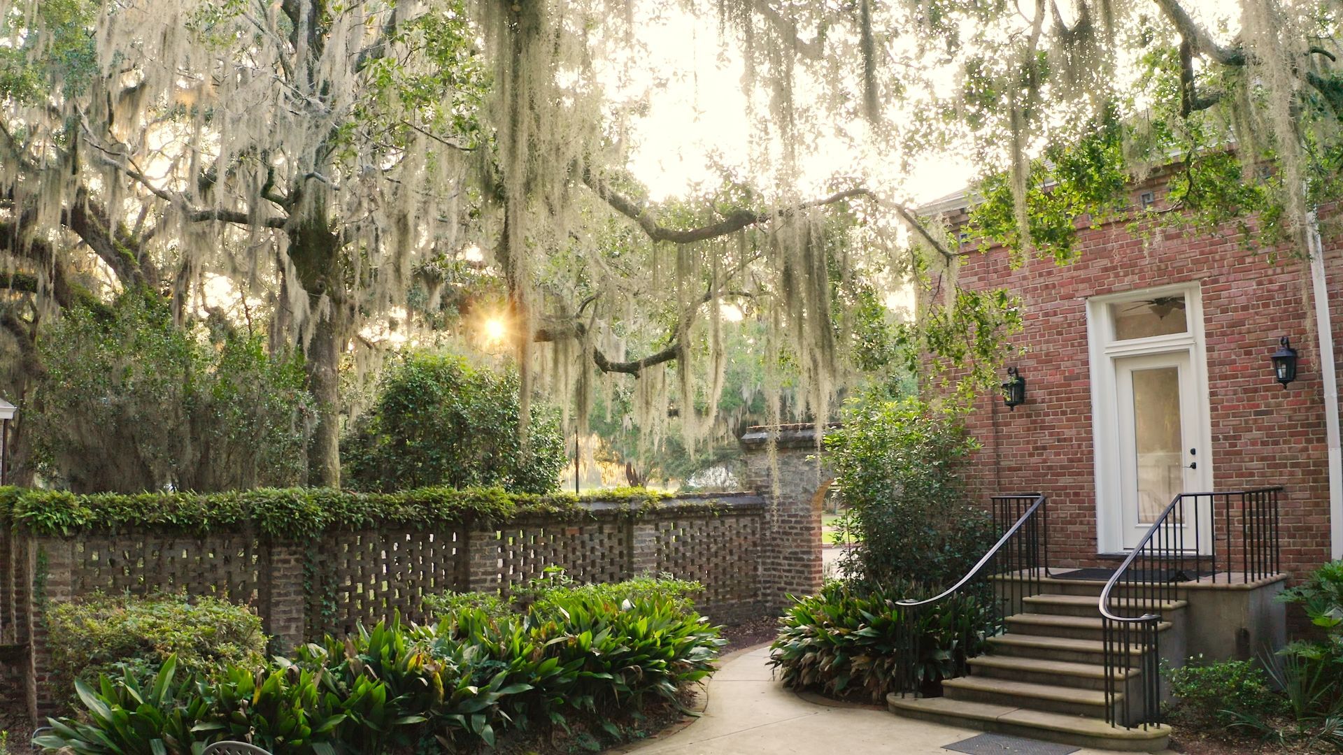 a path leading to a brick building with spanish moss hanging from the trees .