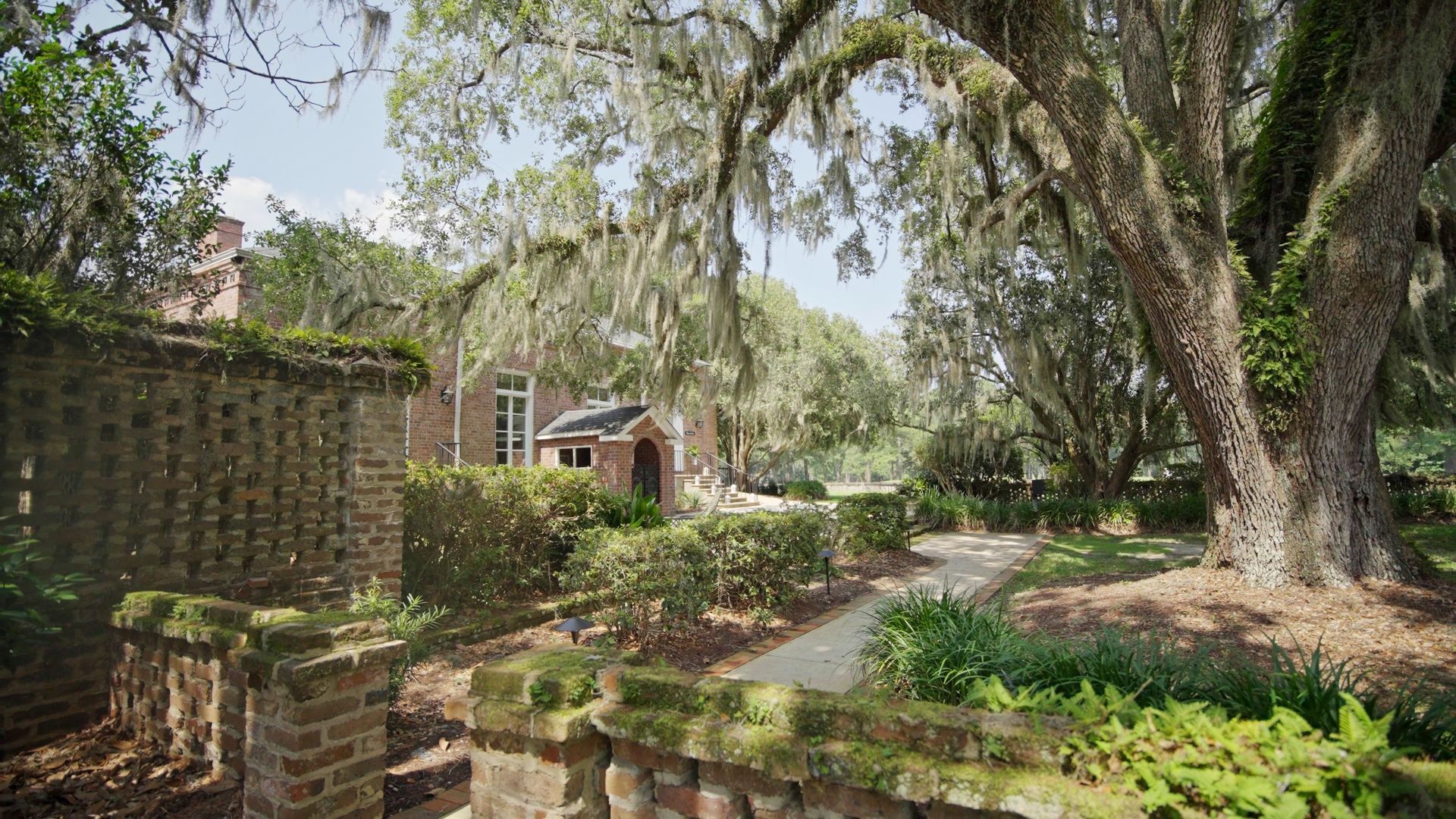 a brick wall surrounded by trees and bushes with a house in the background .