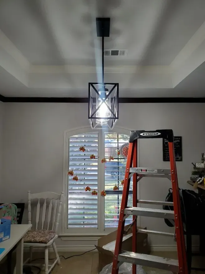 A black pendant light fixture hangs from a white ceiling. A stepladder stands below.