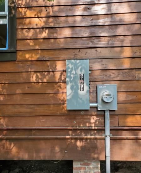 Electrical panel and meter box on a brown wooden building exterior with a gray metal conduit.