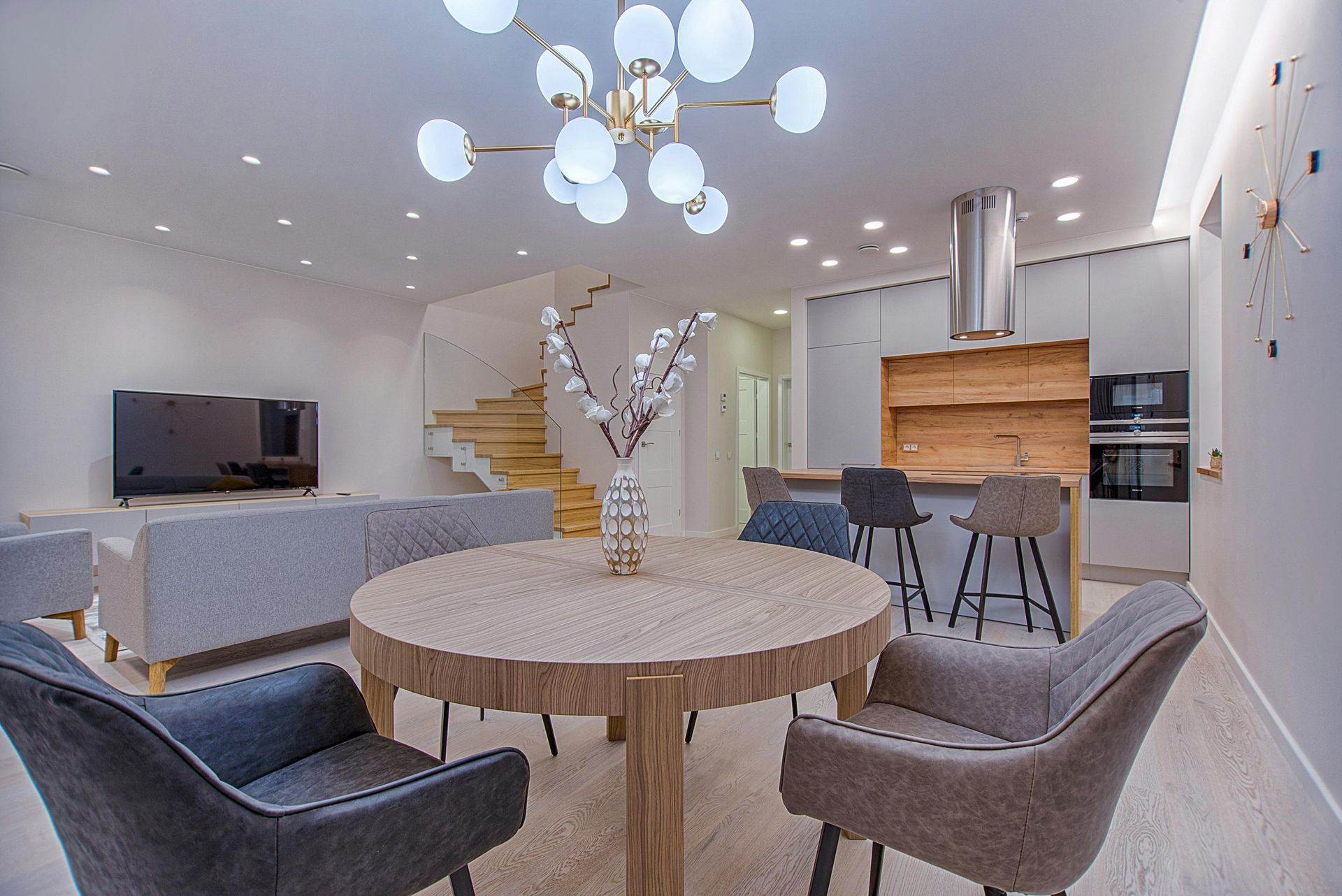 Modern living room with round wooden table, chairs, and a chandelier.