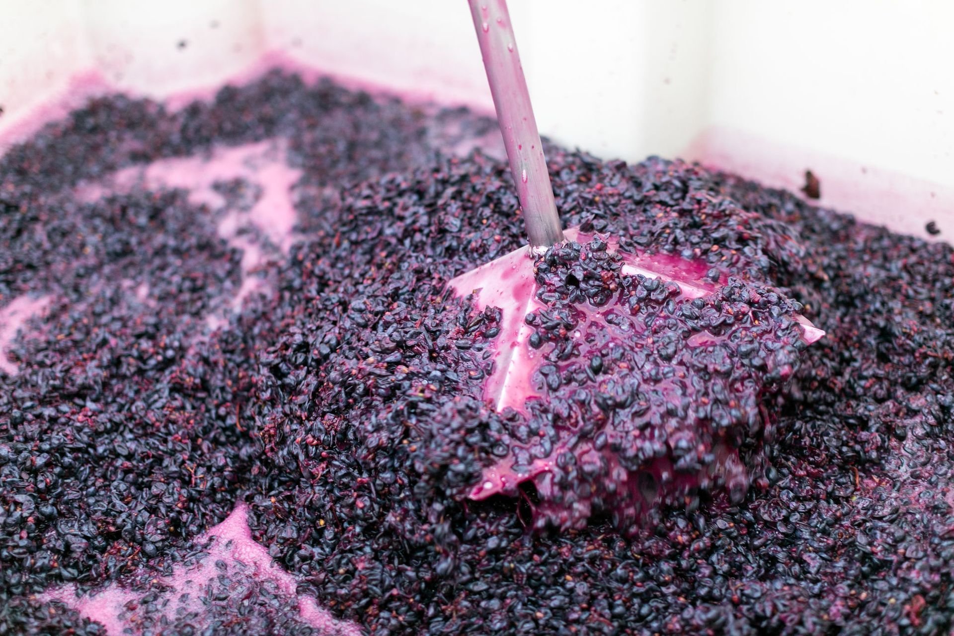 Pink-handled tool stirring dark crushed berries in a bowl