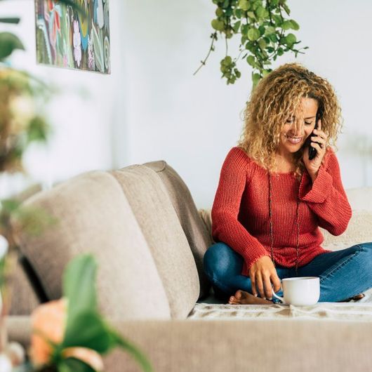 A woman is sitting on a couch talking on a cell phone