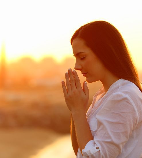 A woman is praying with her hands folded in front of her face.