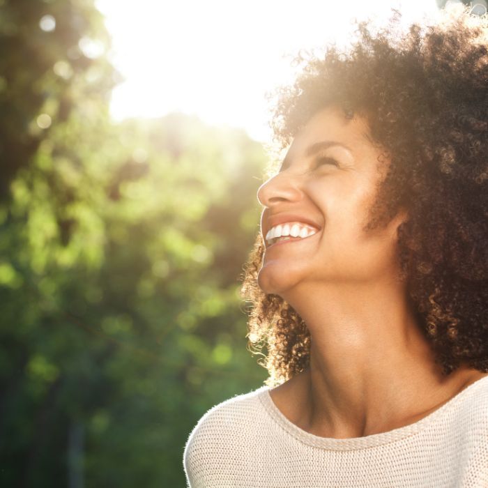 A woman with curly hair is smiling and looking up at the sun.