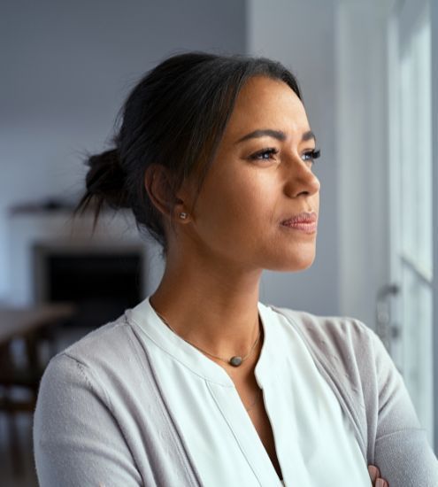 A woman is looking out of a window with her arms crossed.