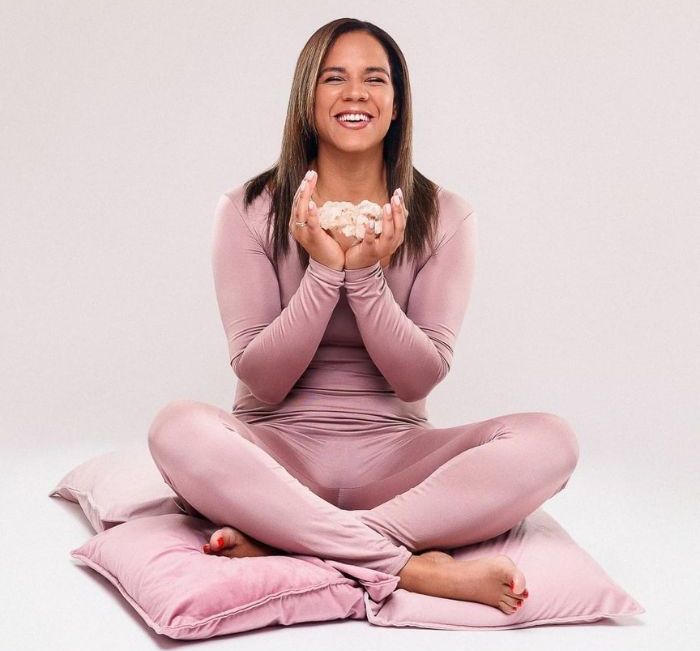 A woman is sitting on a pillow with her legs crossed and holding a bowl of marshmallows.