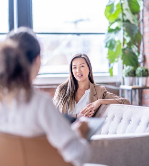 A woman is sitting on a couch talking to another woman.