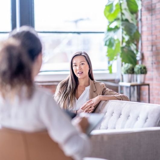 A woman is sitting on a couch talking to another woman.