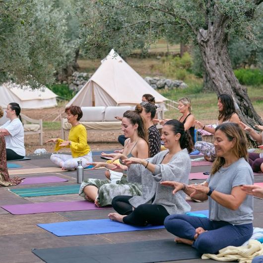 A group of women are sitting on yoga mats in front of a tent