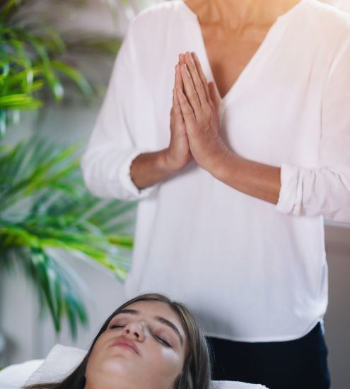 A woman in a white shirt is praying over a woman laying on a bed.