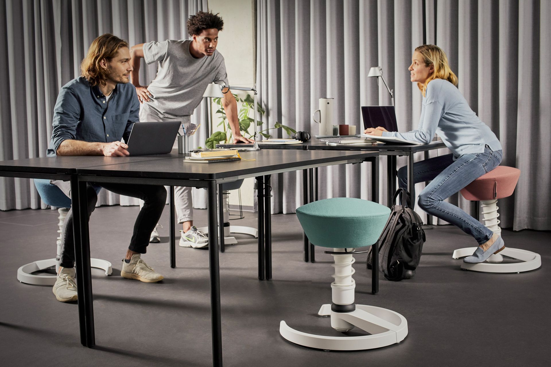 Zwei Personen im Gespräch an einem höhenverstellbaren Tisch mit Swopper-Hockern
