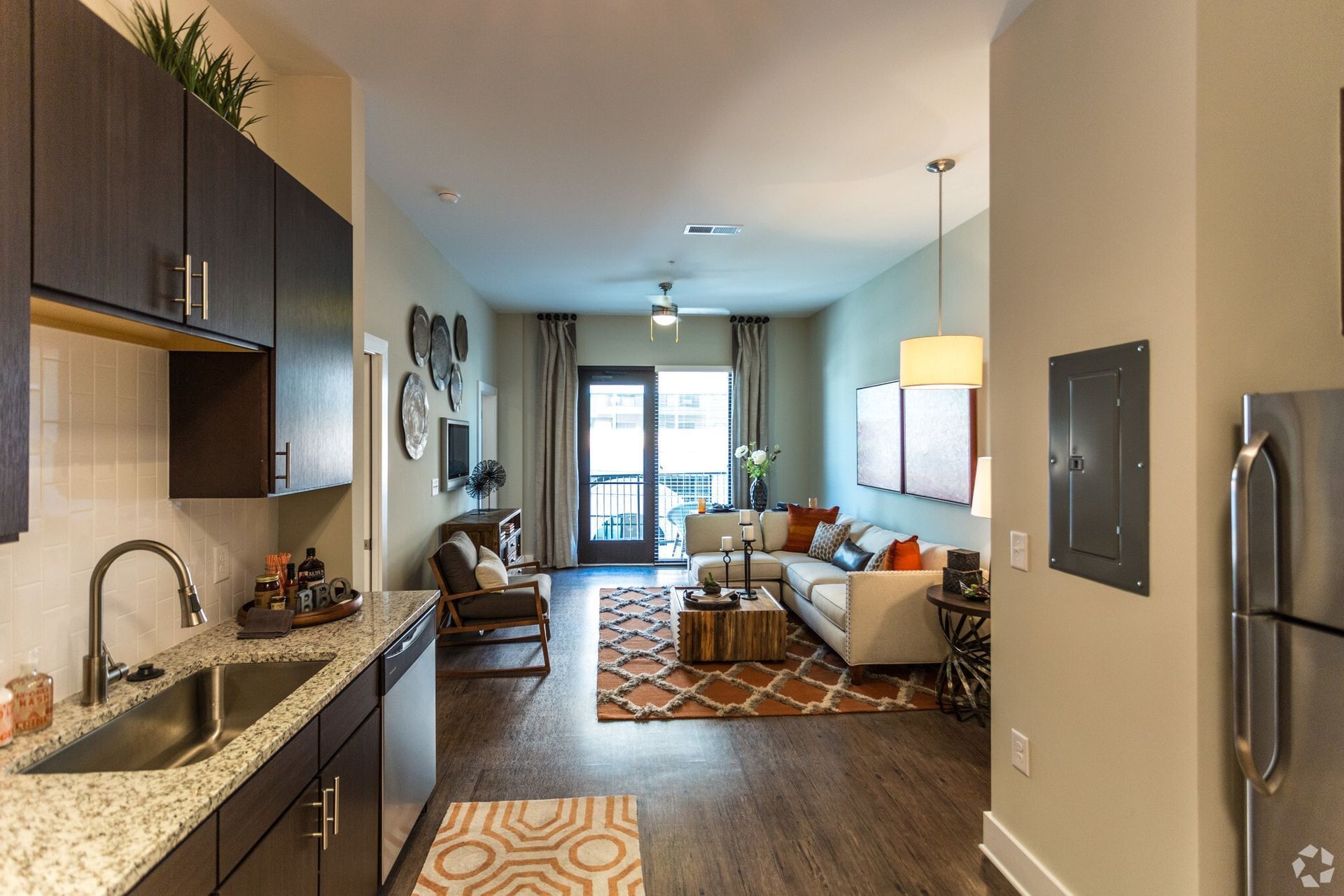 Open-concept living area with dark kitchen cabinets, granite counters, and a beige sofa by the balcony.