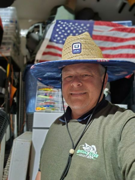 A man wearing a straw hat is standing in front of an american flag