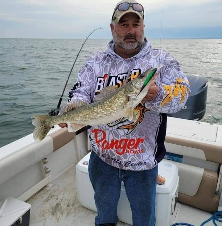 A man wearing a blaster shirt is holding a large fish