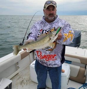 A man wearing a blaster shirt is holding a large fish