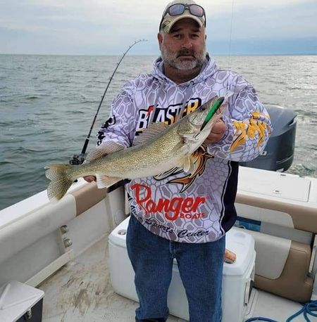 A man wearing a blaster shirt is holding a large fish