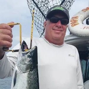 A man wearing sunglasses and a hat with the word papa on it is holding a fish