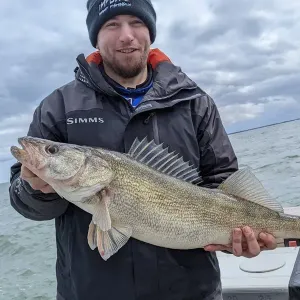 A man in a simms jacket is holding a large fish in his hands.