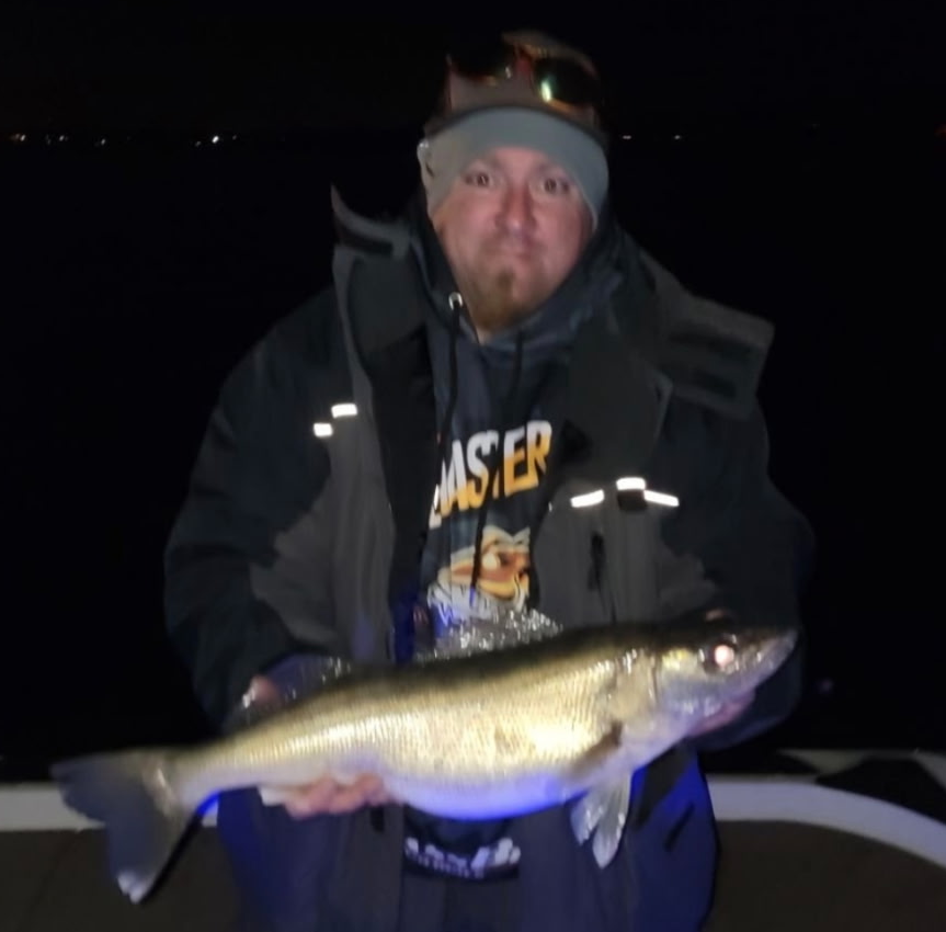 A person is holding a fish with a fly in its mouth.