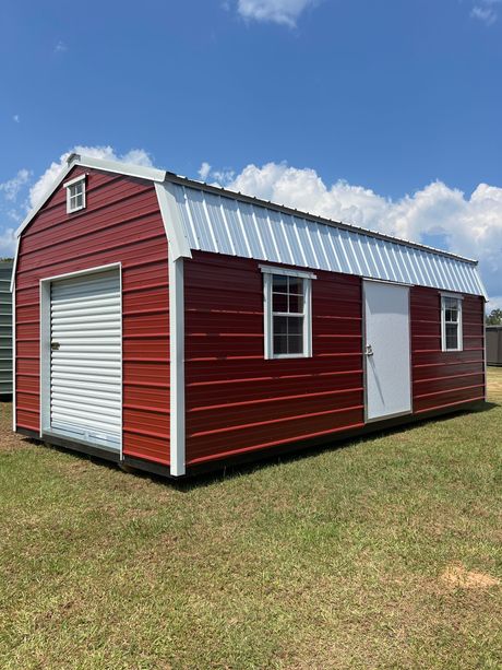 Red barn-style shed with white trim and a metal roof; a garage door, windows, and a door are visible on the exterior.