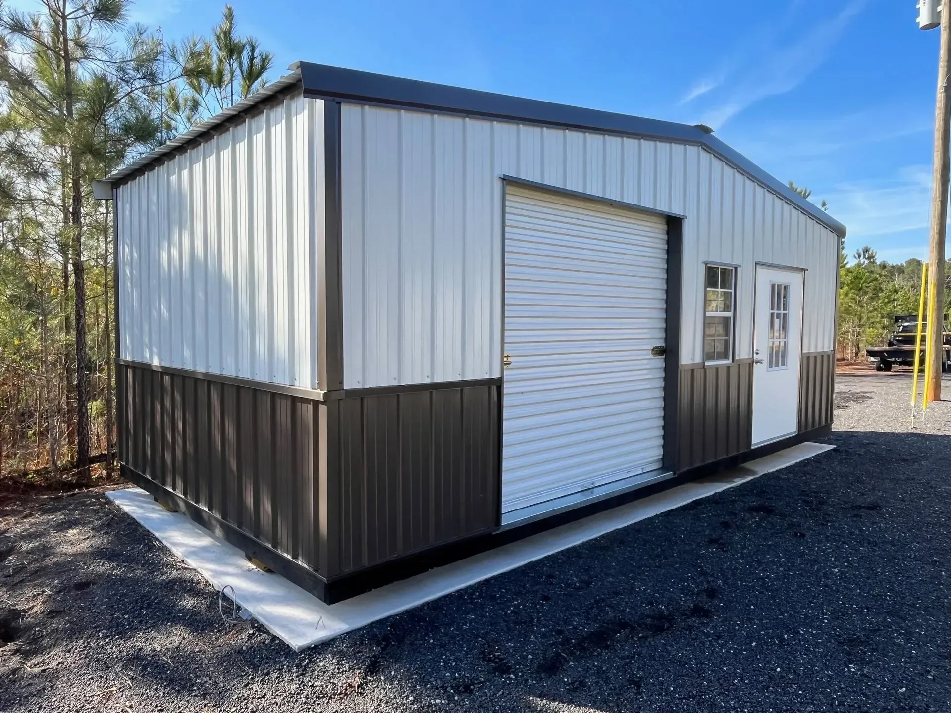 Metal shed with white and brown panels, a garage door, and a side door on a concrete foundation.