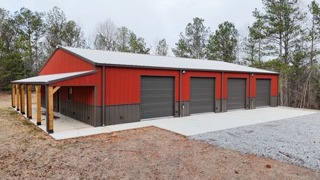 An aerial view of a red barn with a white roof and a driveway surrounded by trees.
