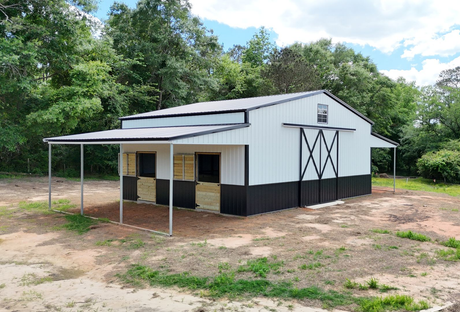 A white and black barn with a covered porch in a field.