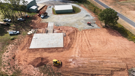 Aerial view of construction site with machines and a building. Earth-toned with vehicles, gravel, and an ongoing project.