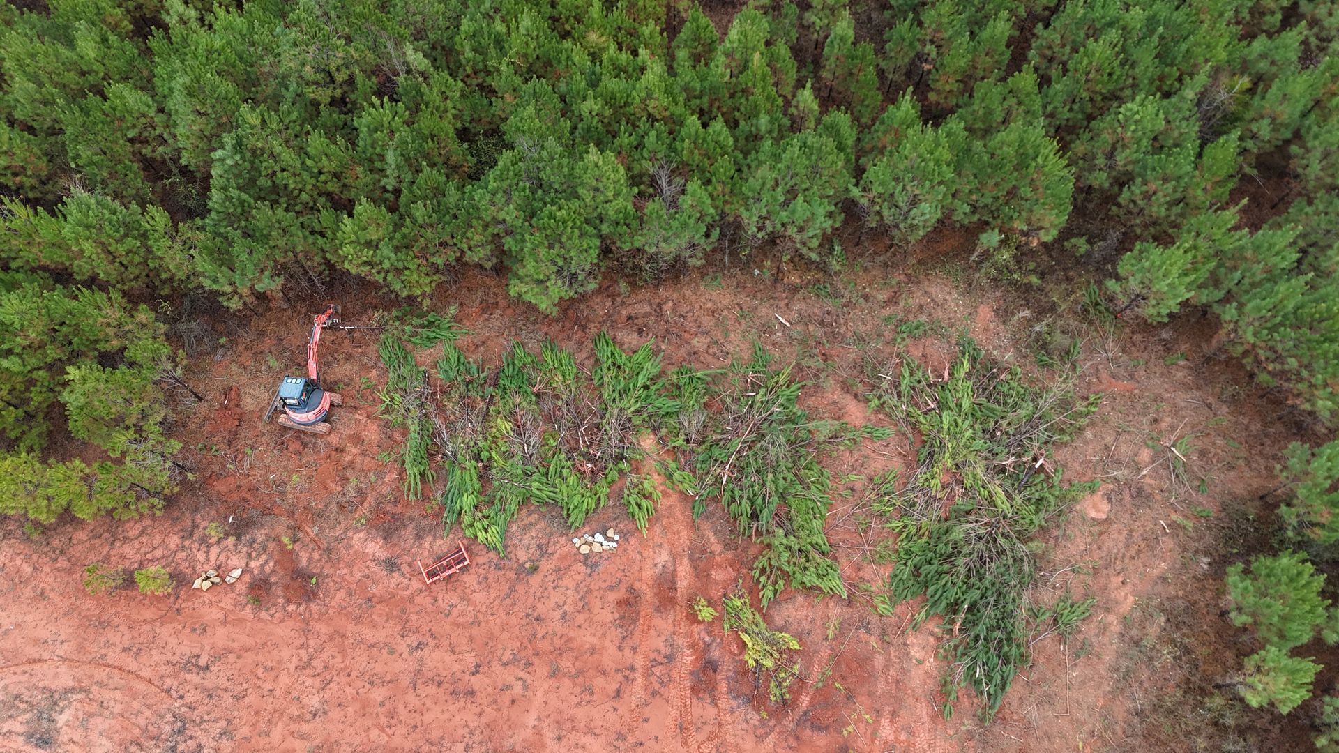 Aerial view of a clearing being made in a forest by an excavator, brown earth and green trees.