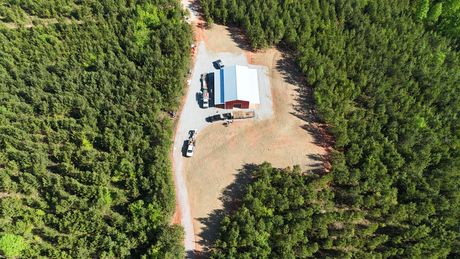 Aerial view of a building and vehicles in a clearing surrounded by dense green forest.
