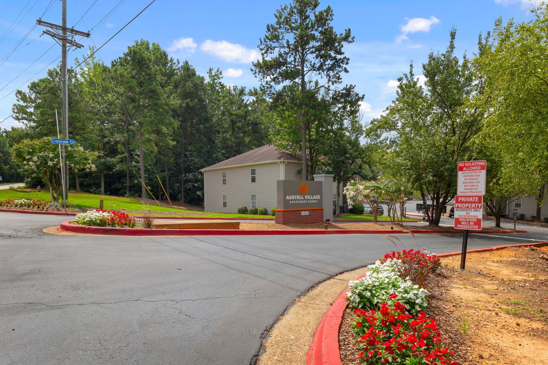Entrance to the Bellington Court apartment complex with a red-bordered driveway, landscaping, and signage on a sunny day.