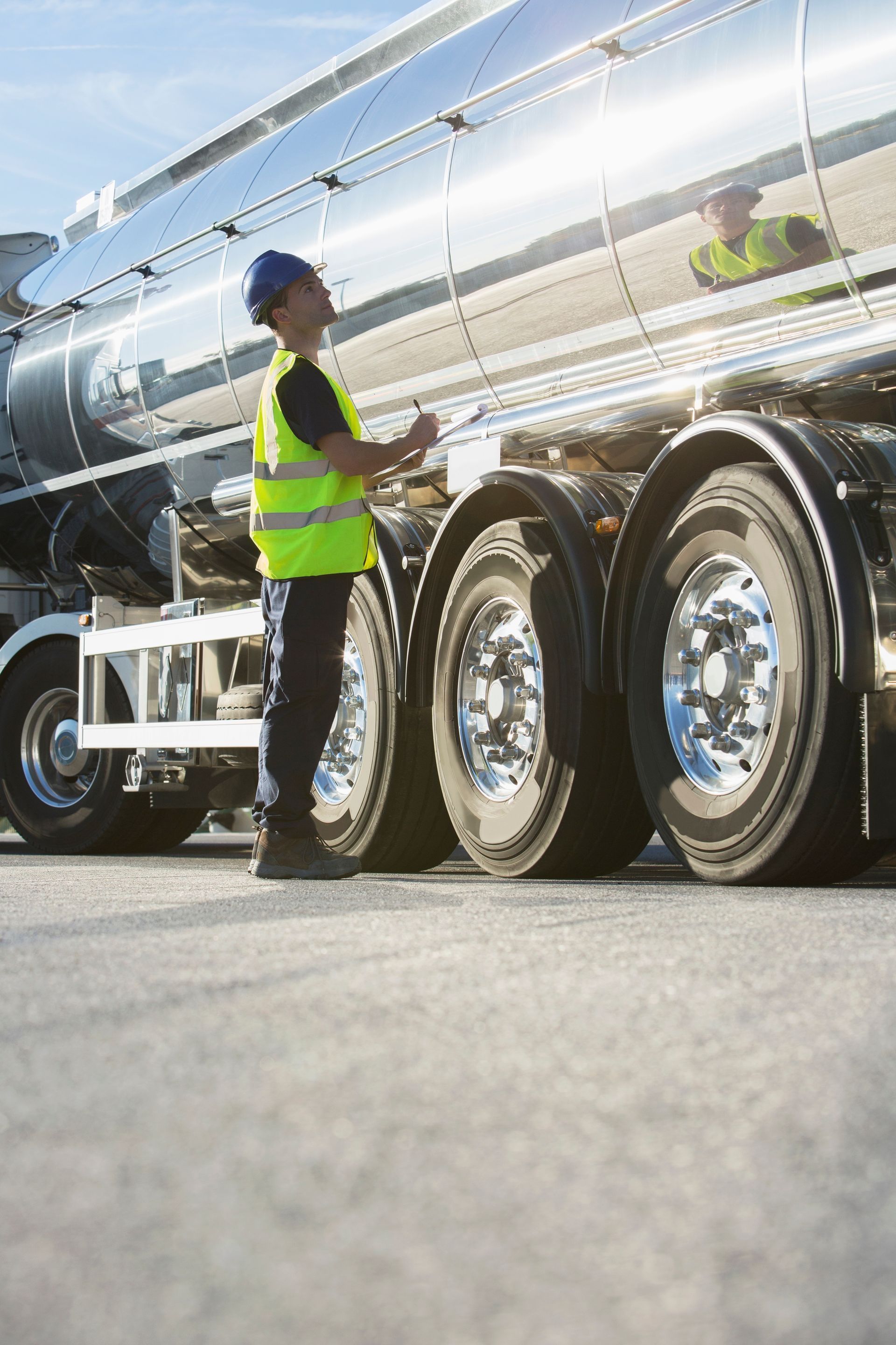 A man in a yellow vest is standing next to a large tanker truck.