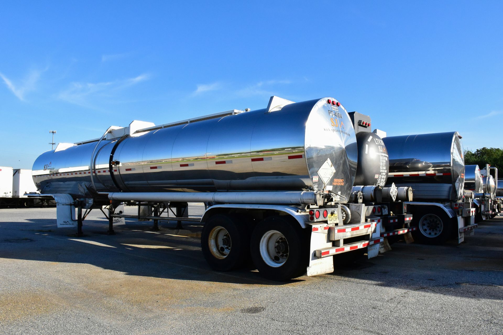 A row of stainless steel tanker trucks are parked in a parking lot.