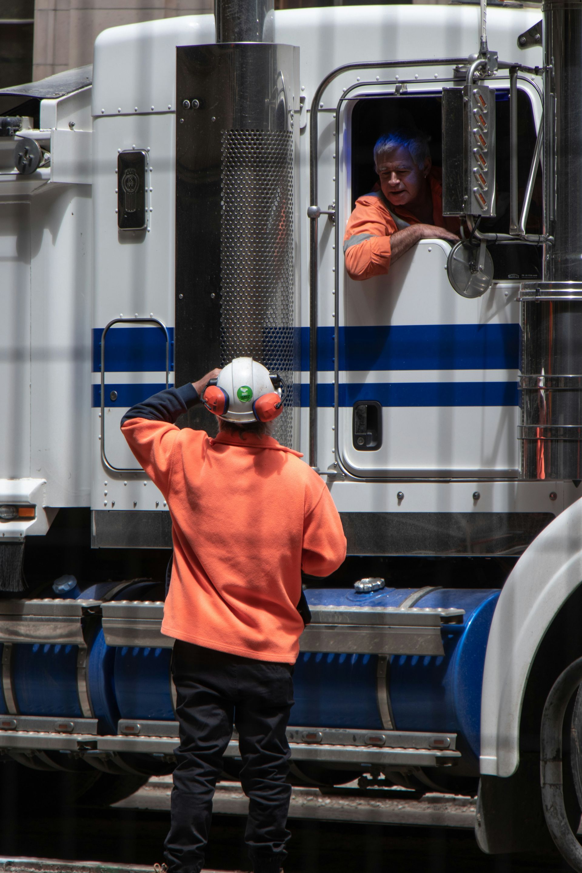 A man in an orange shirt stands in front of a semi truck