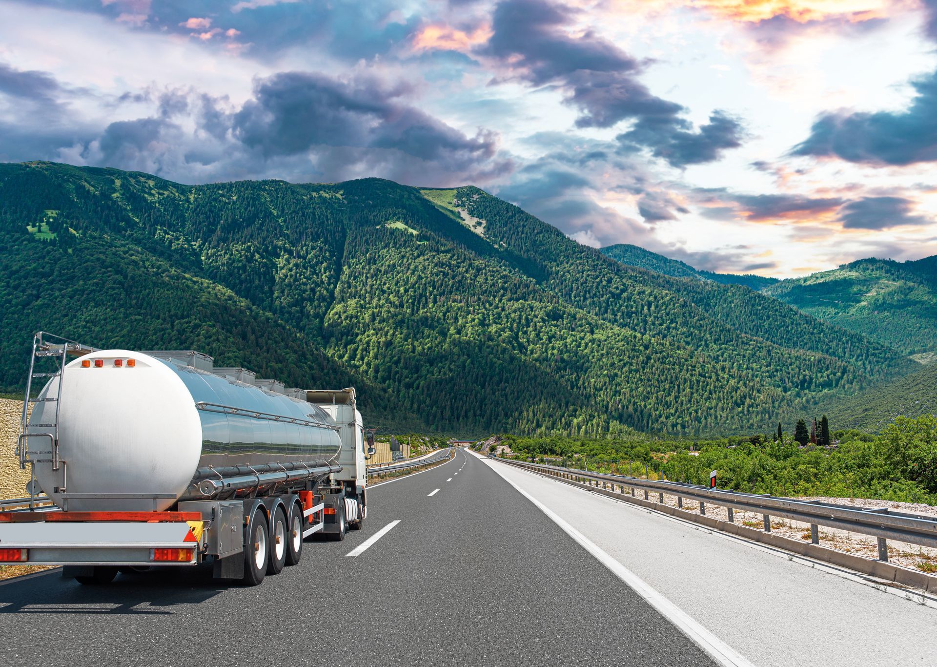A tanker truck is driving down a highway with mountains in the background.