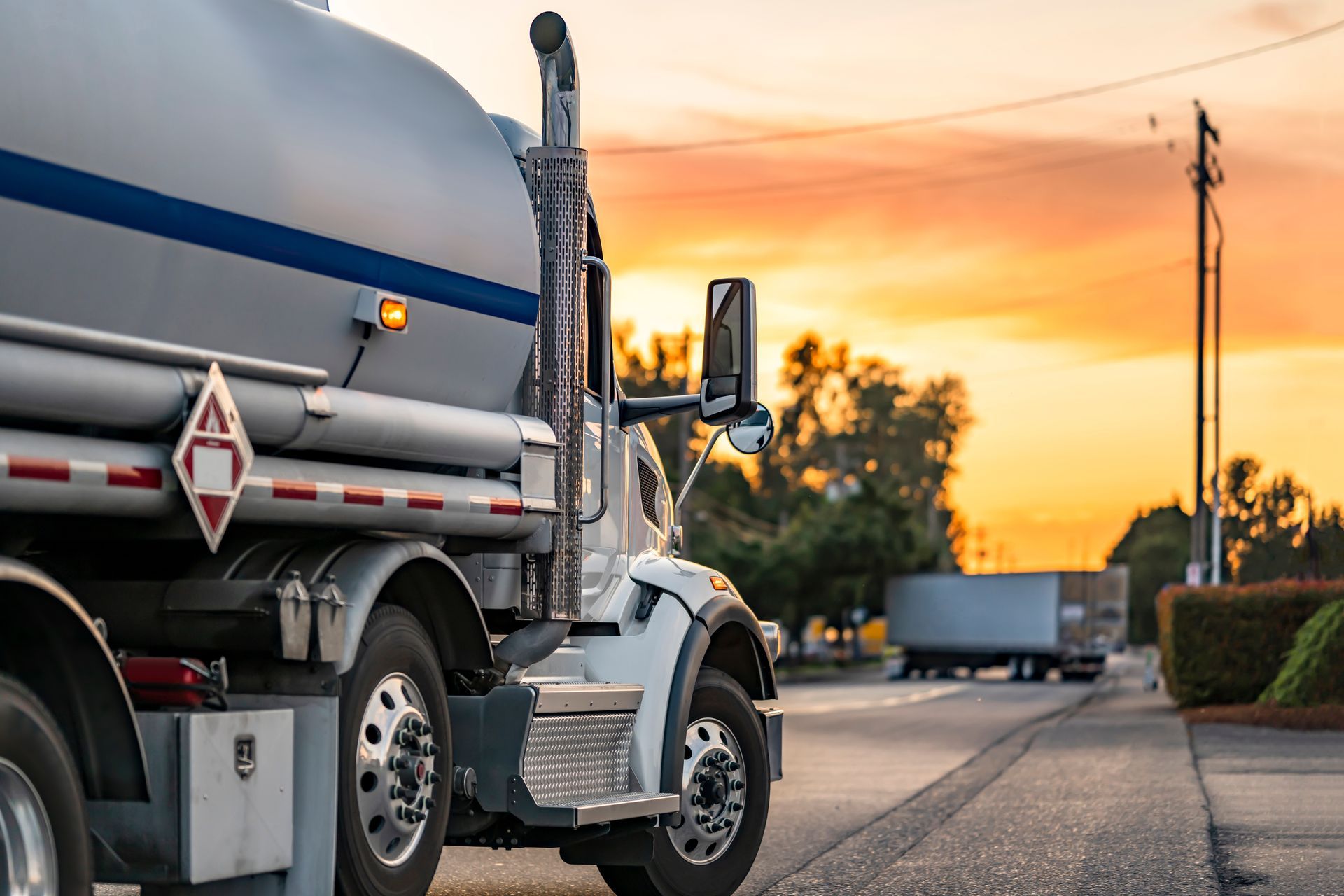 A tanker truck is parked on the side of the road at sunset.