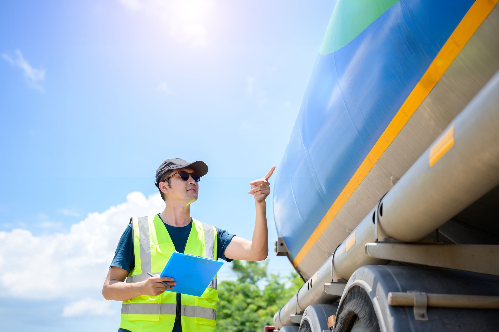A man is standing next to a tanker truck holding a clipboard and pointing at it.