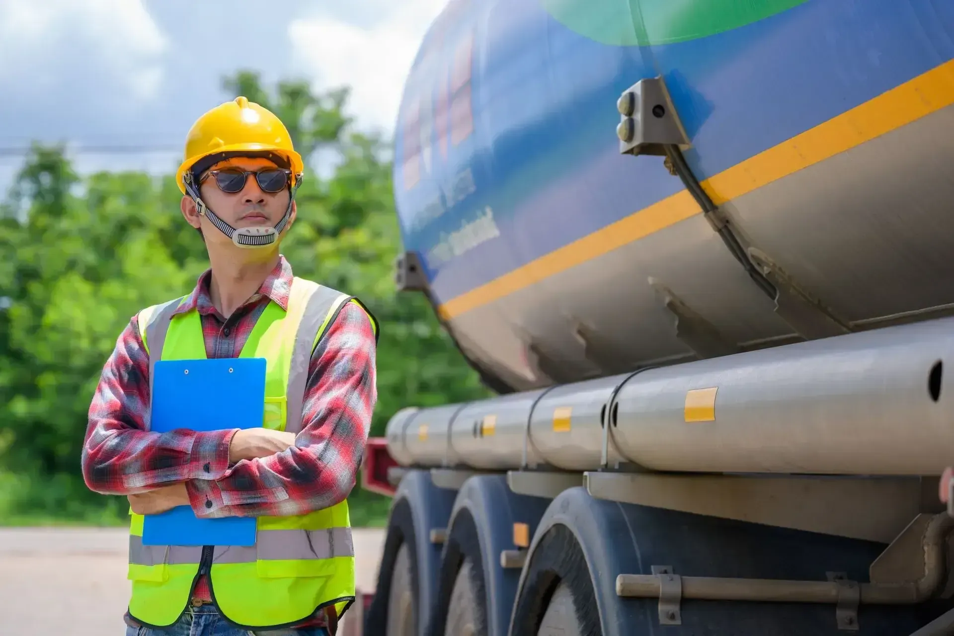 A man in a hard hat and safety vest is standing next to a tanker truck.