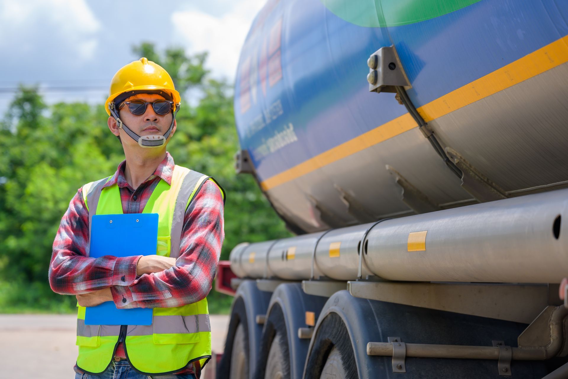 A man in a hard hat and safety vest is standing next to a tanker truck.