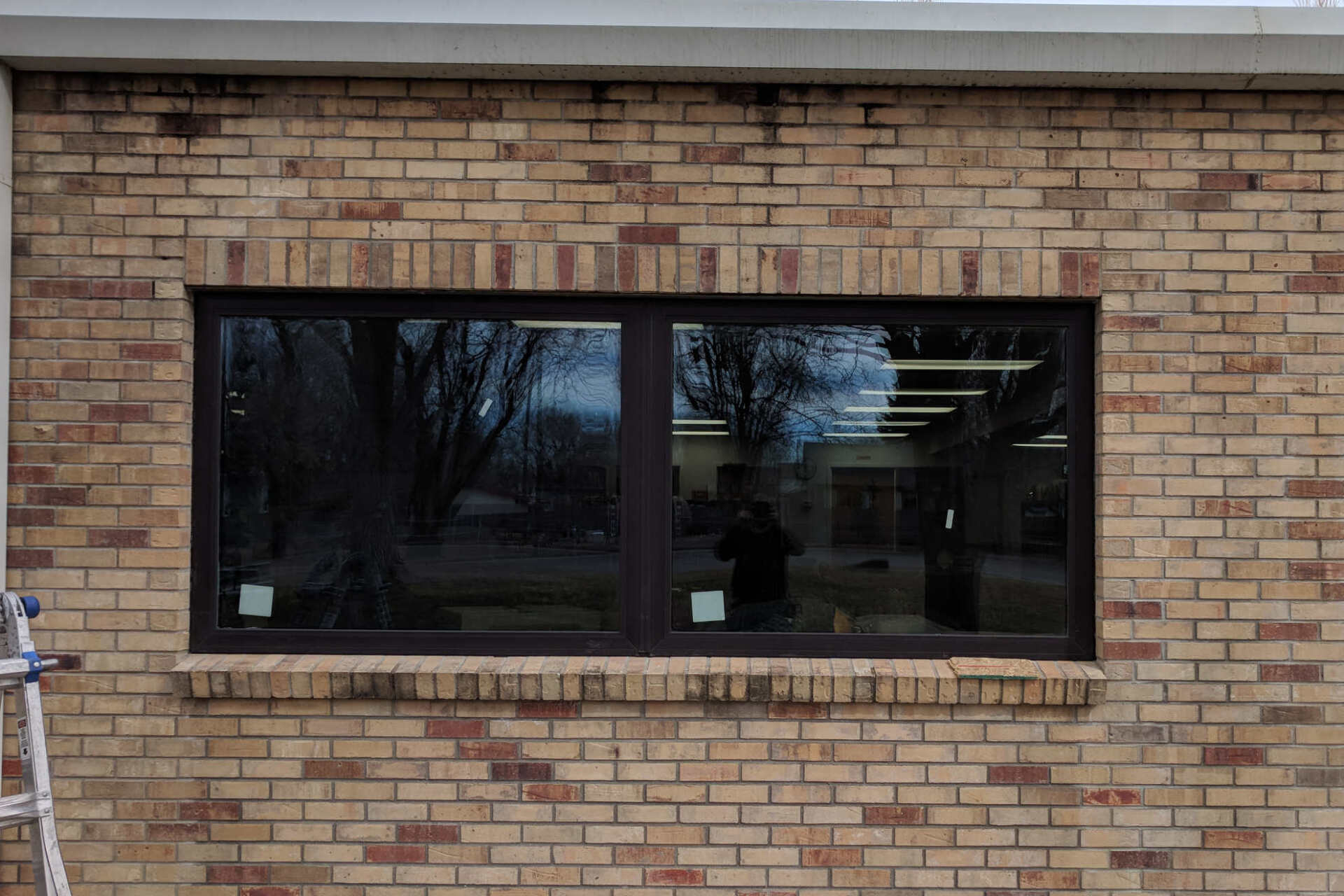 A brick building with a large window and a ladder in front of it.