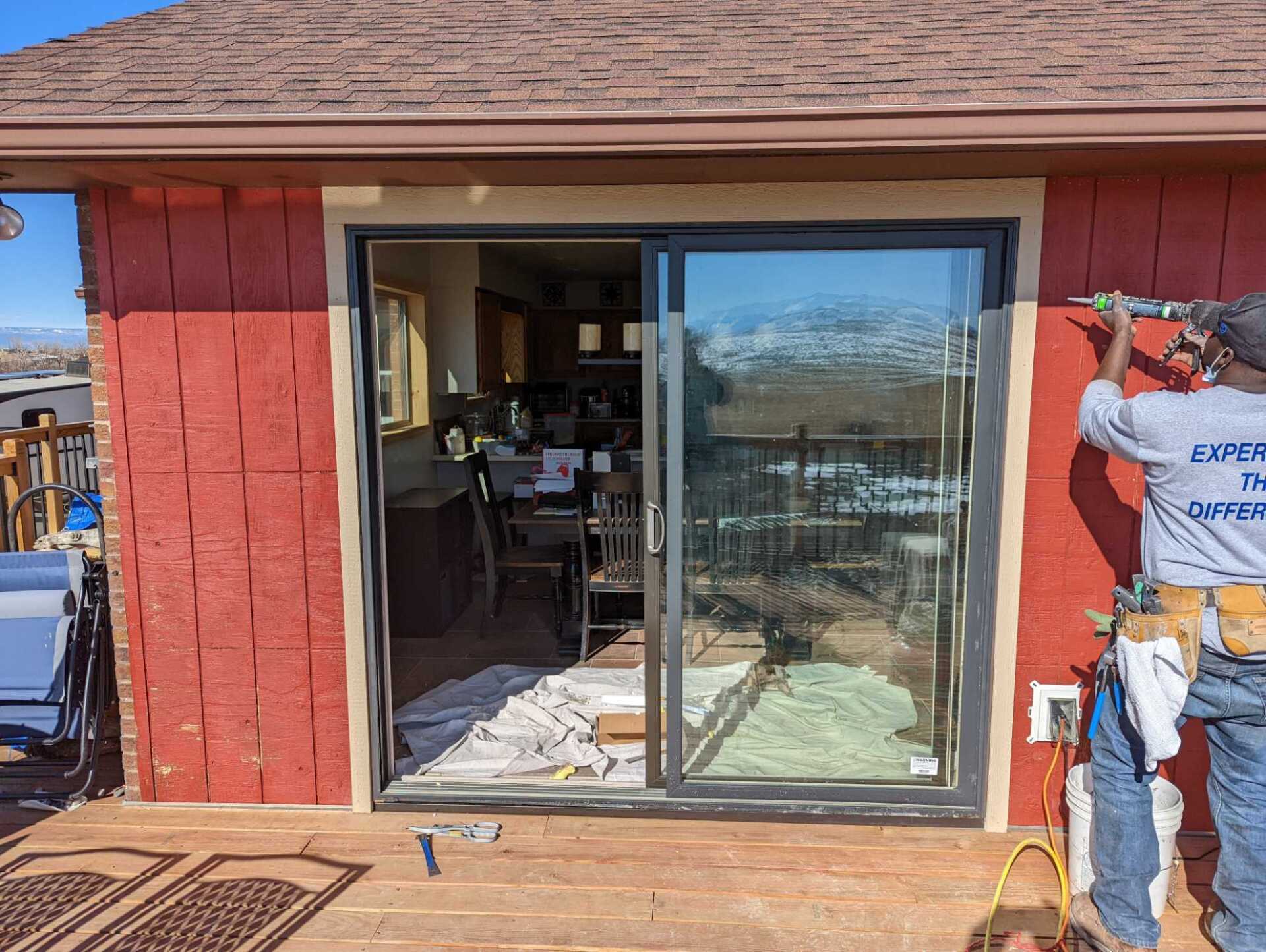 A man is installing a sliding glass door on a red house.