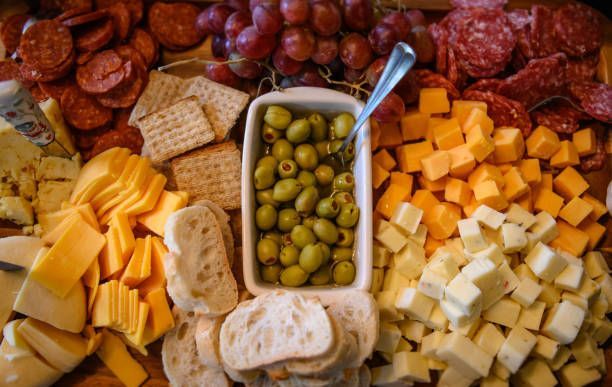 A tray of cheese , crackers , olives , grapes and salami on a table.
