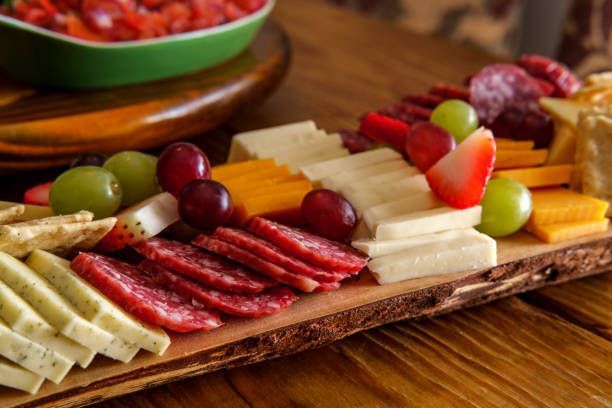 A wooden cutting board filled with cheese , grapes , and salami.
