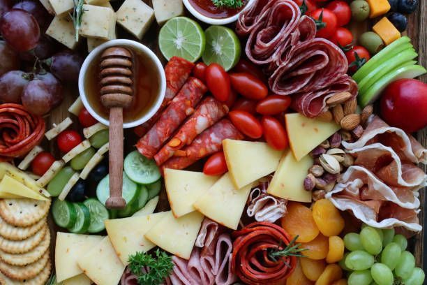 A variety of fruits , cheeses , meats , vegetables and crackers on a wooden table.