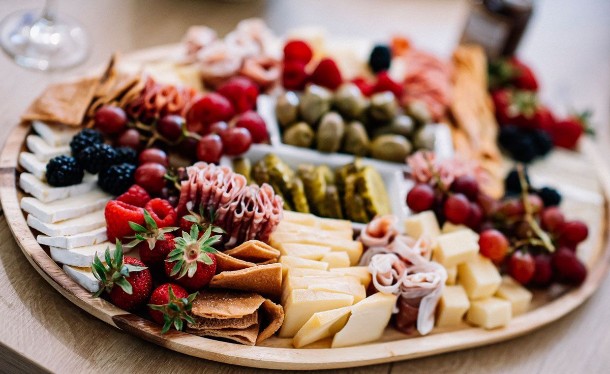 A wooden cutting board filled with cheese , fruit , crackers and olives.