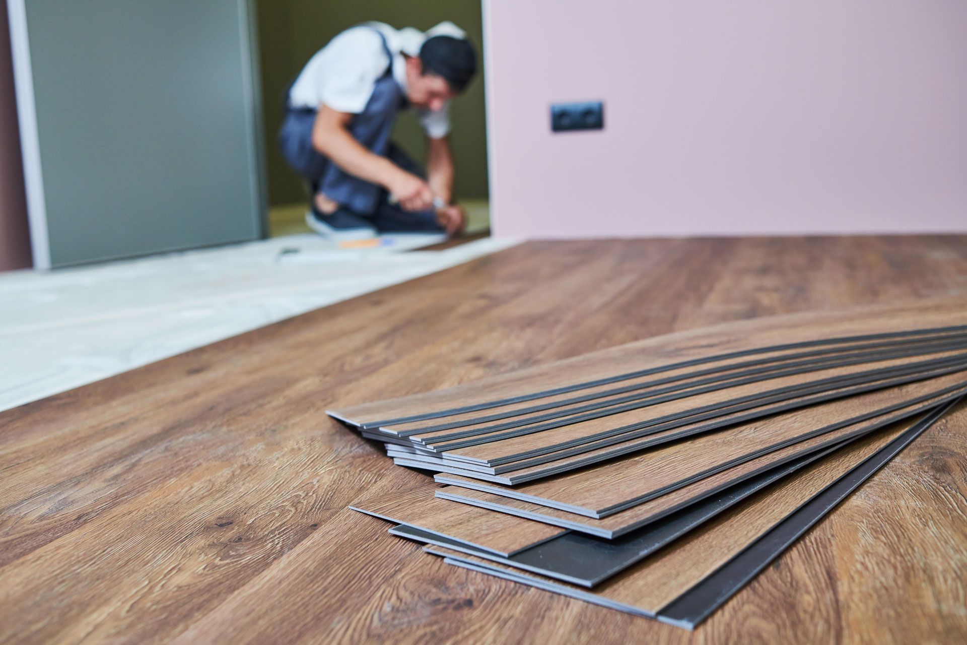 Man installing wood-look flooring; planks in foreground, room in background.