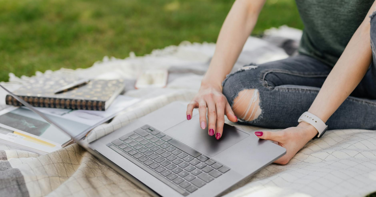 A woman is sitting on a blanket using a laptop computer.