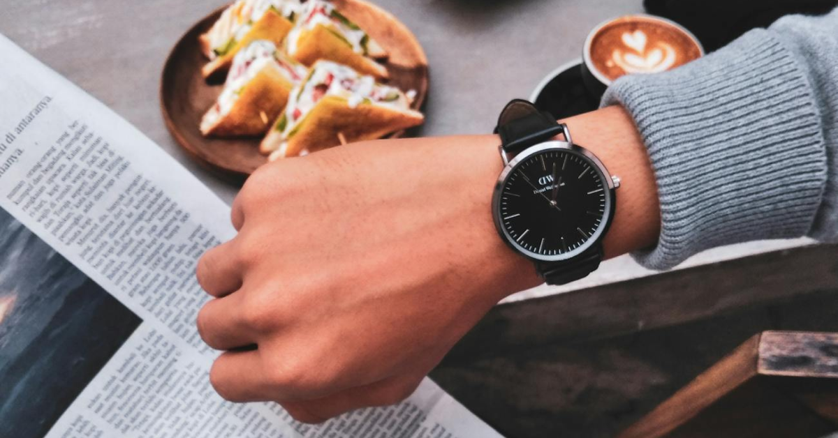 A person wearing a watch is looking at their watch while reading a newspaper.